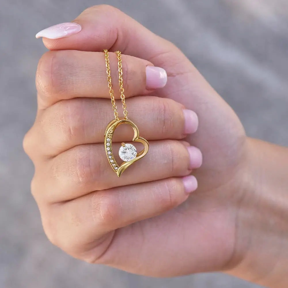 Gold heart-shaped necklace with a diamond held in a hand against a neutral background
